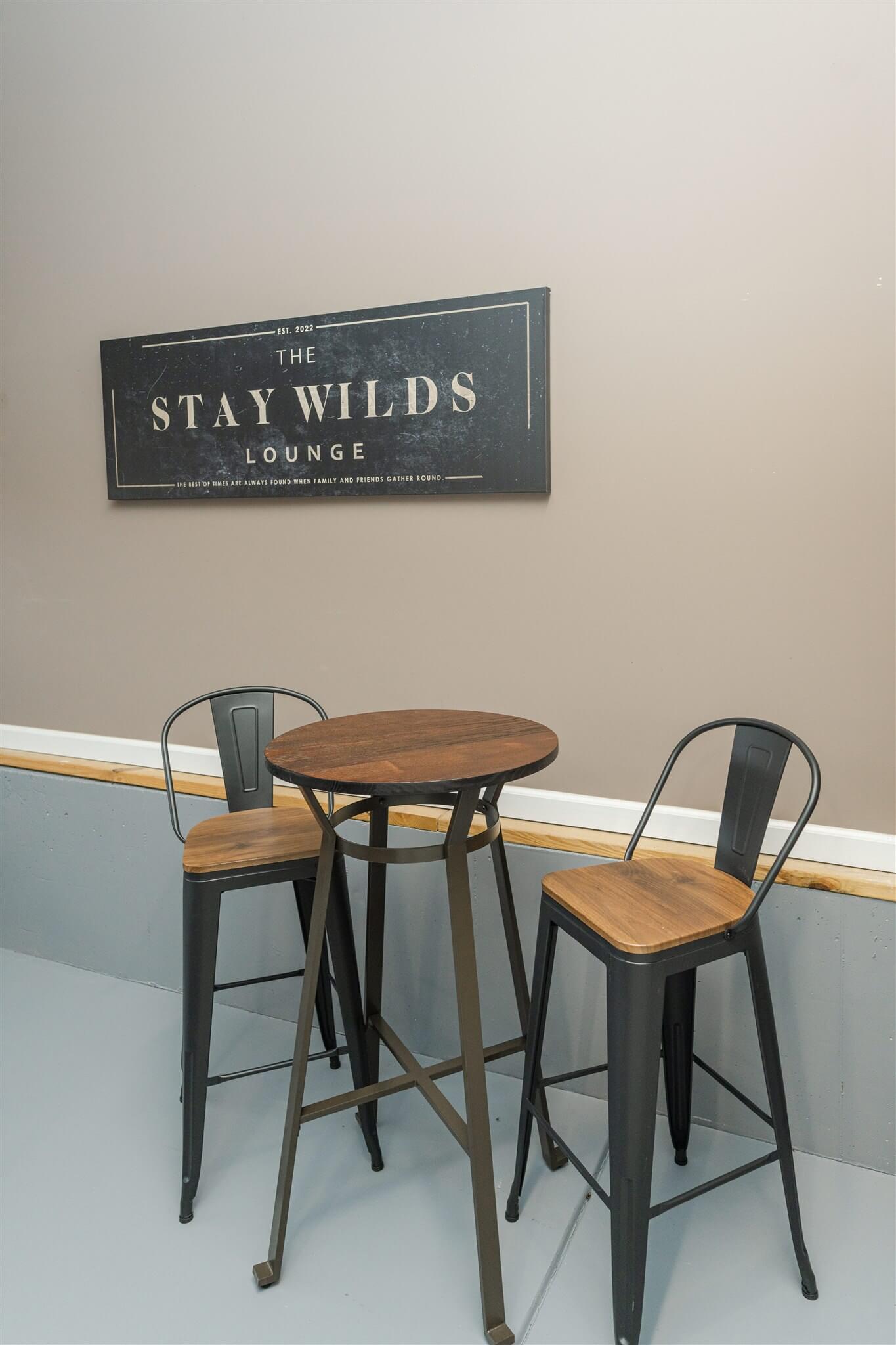 High-top table and stools under Stay Wilds Lounge sign